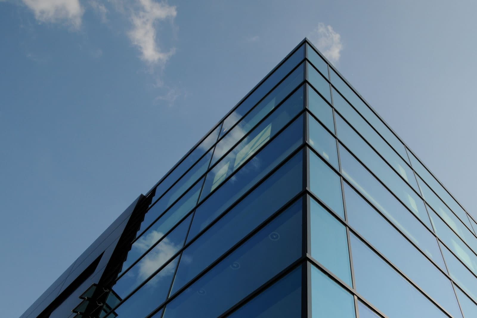 Ecksicht auf ein modernes Glasgebäude mit reflektierendem blauen Himmel und Wolken.